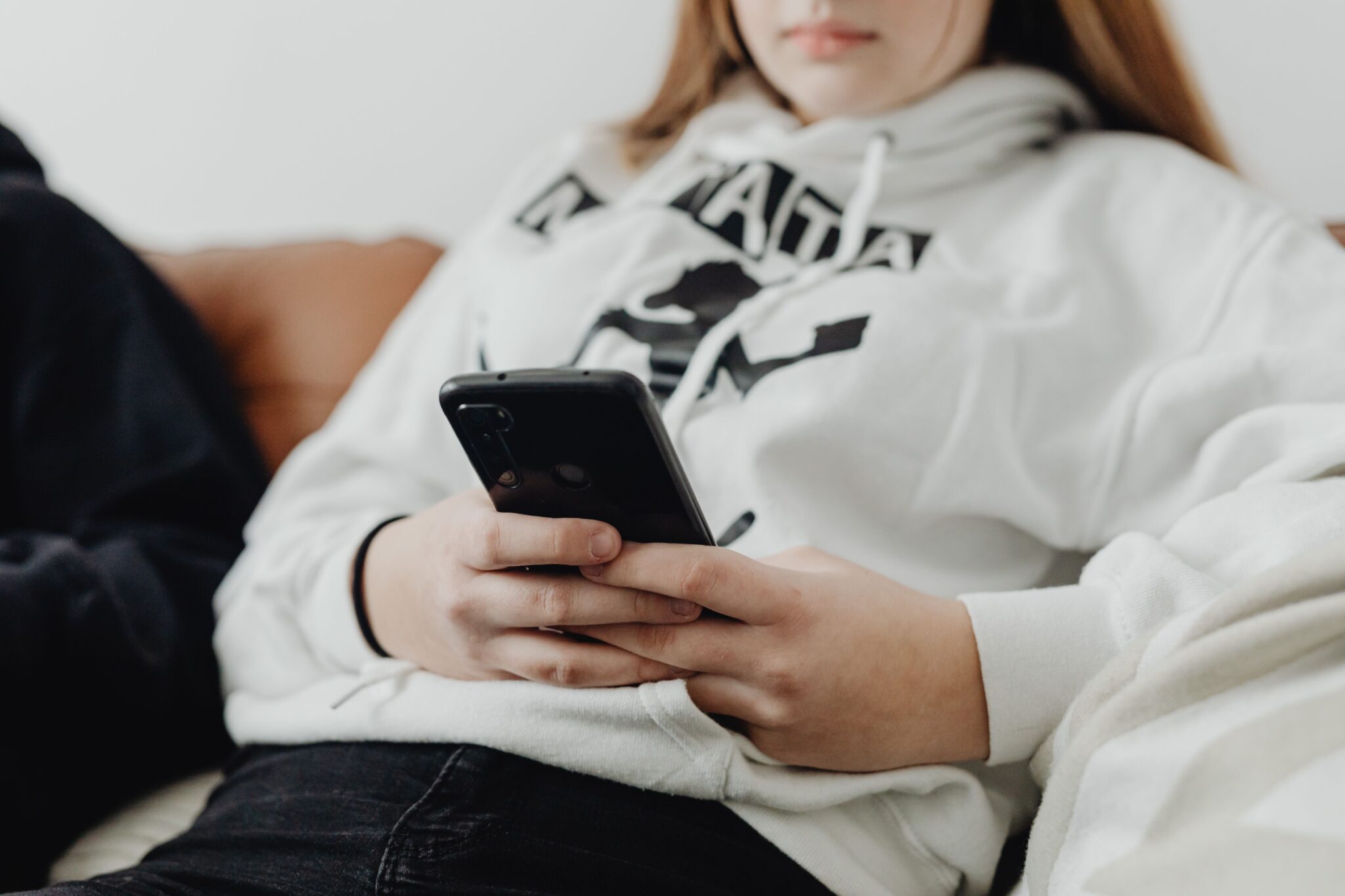 Teenage girl using smartphone while relaxing on a sofa, depicting leisure and connectivity.